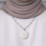 Silver Al-Qadīr Necklace worn by a modest woman, featuring Arabic calligraphy meaning “And He is capable of all things,” styled with a neutral hijab and white top.
