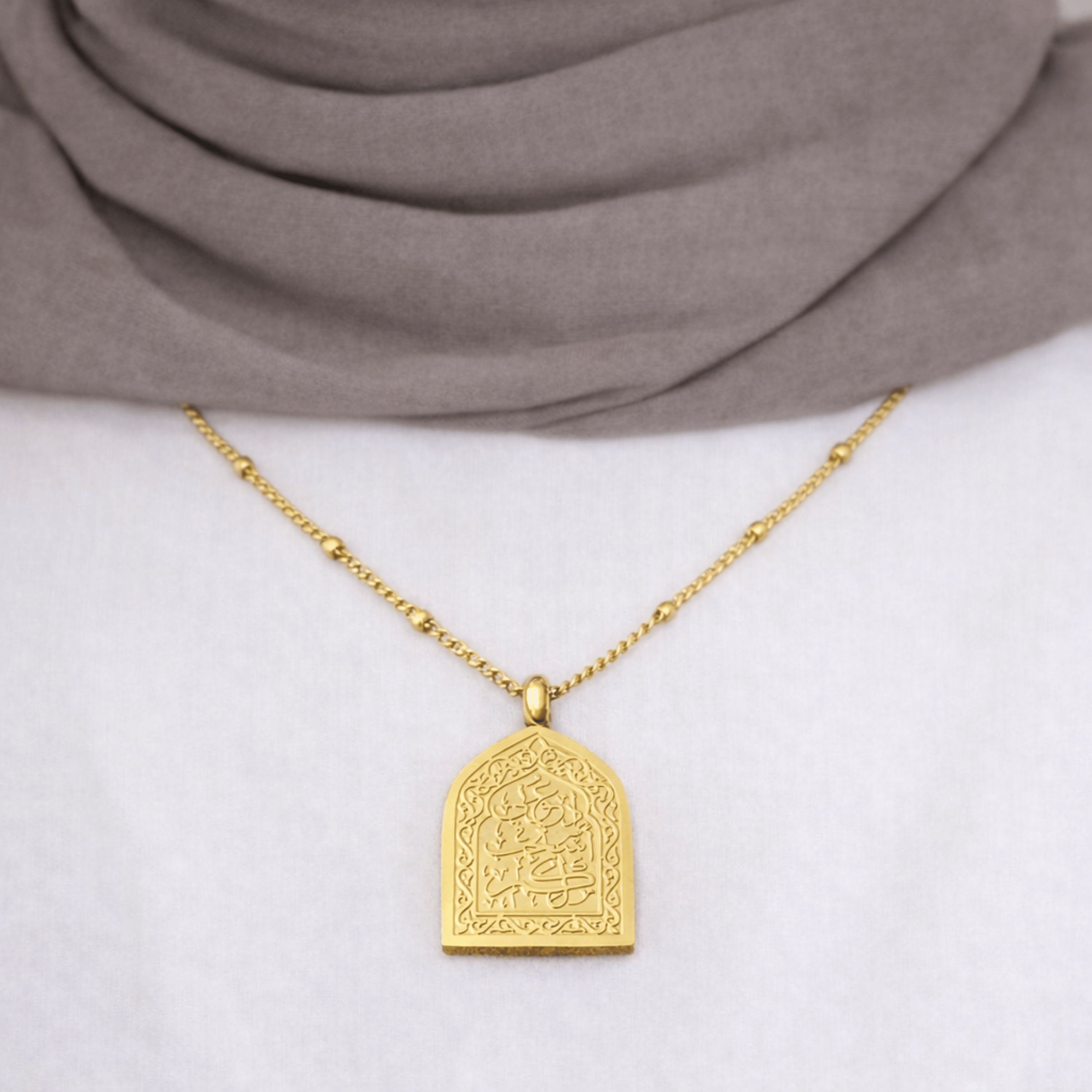 Gold Ud‘ooni Necklace worn by a modest woman, featuring Quran verse “Call Upon Me, I Will Respond,” shown styled over a white top and neutral hijab.